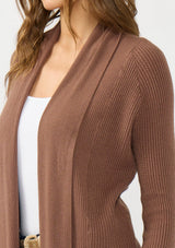 [Color: Clove] A detail image of a Lovestitch model wearing a chic brown waffle knit wrap front sweater with long sleeves, a v neckline, and a button closure at the back. The long ties can be styled in multiple ways.