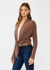 [Color: Clove] A side facing image of a Lovestitch model wearing a chic brown waffle knit wrap front sweater with long sleeves, a v neckline, and a button closure at the back. The long ties can be styled in multiple ways.