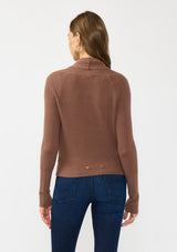 [Color: Clove] A back facing image of a Lovestitch model wearing a chic brown waffle knit wrap front sweater with long sleeves, a v neckline, and a button closure at the back. The long ties can be styled in multiple ways.