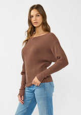 [Color: Clove] A side facing image of a brunette model wearing a brown waffle knit pullover sweater. With long sleeves, a relaxed fit, and a wide neckline that can be worn off the shoulder.