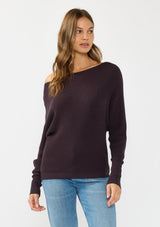[Color: Aubergine] A front facing image of a brunette model wearing a dark purple waffle knit pullover sweater. With long sleeves, a relaxed fit, and a wide neckline that can be worn off the shoulder.