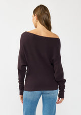 [Color: Aubergine] A back facing image of a brunette model wearing a dark purple waffle knit pullover sweater. With long sleeves, a relaxed fit, and a wide neckline that can be worn off the shoulder.