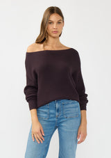 [Color: Aubergine] A front facing image of a brunette model wearing a dark purple waffle knit pullover sweater. With long sleeves, a relaxed fit, and a wide neckline that can be worn off the shoulder.