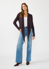 [Color: Aubergine] A front facing image of a Lovestitch model wearing a chic dark purple waffle knit wrap front sweater with long sleeves, a v neckline, and a button closure at the back. The long ties can be styled in multiple ways.