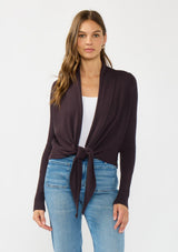 [Color: Aubergine] A photo of a Lovestitch model wearing a chic dark purple waffle knit wrap front sweater with long sleeves, a v neckline, and a button closure at the back. The long ties can be styled in multiple ways.