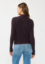 [Color: Aubergine] A back facing image of a Lovestitch model wearing a chic dark purple waffle knit wrap front sweater with long sleeves, a v neckline, and a button closure at the back. The long ties can be styled in multiple ways.