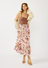 [Color: Almond/Wine] A front facing image of a blonde model wearing a convertible pink floral print skirt with a smocked waist and a ruffle trimmed hem. 