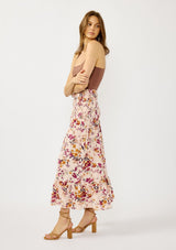 [Color: Almond/Wine] A side facing image of a blonde model wearing a convertible pink floral print skirt with a smocked waist and a ruffle trimmed hem. 