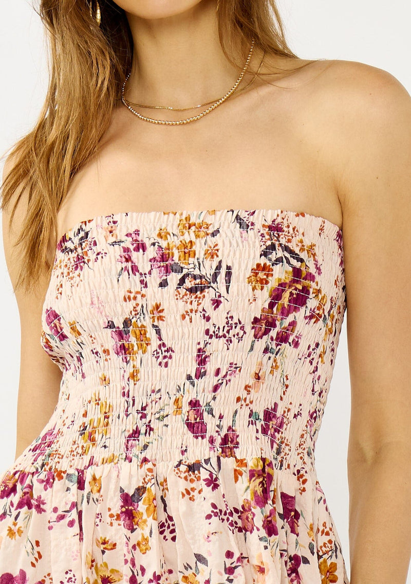 [Color: Almond/Wine] A detail image of a blonde model wearing a convertible pink floral print midi dress with a smocked bodice and a ruffle trimmed hem. 