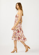 [Color: Almond/Wine] A side facing image of a blonde model wearing a convertible pink floral print midi dress with a smocked bodice and a ruffle trimmed hem. 