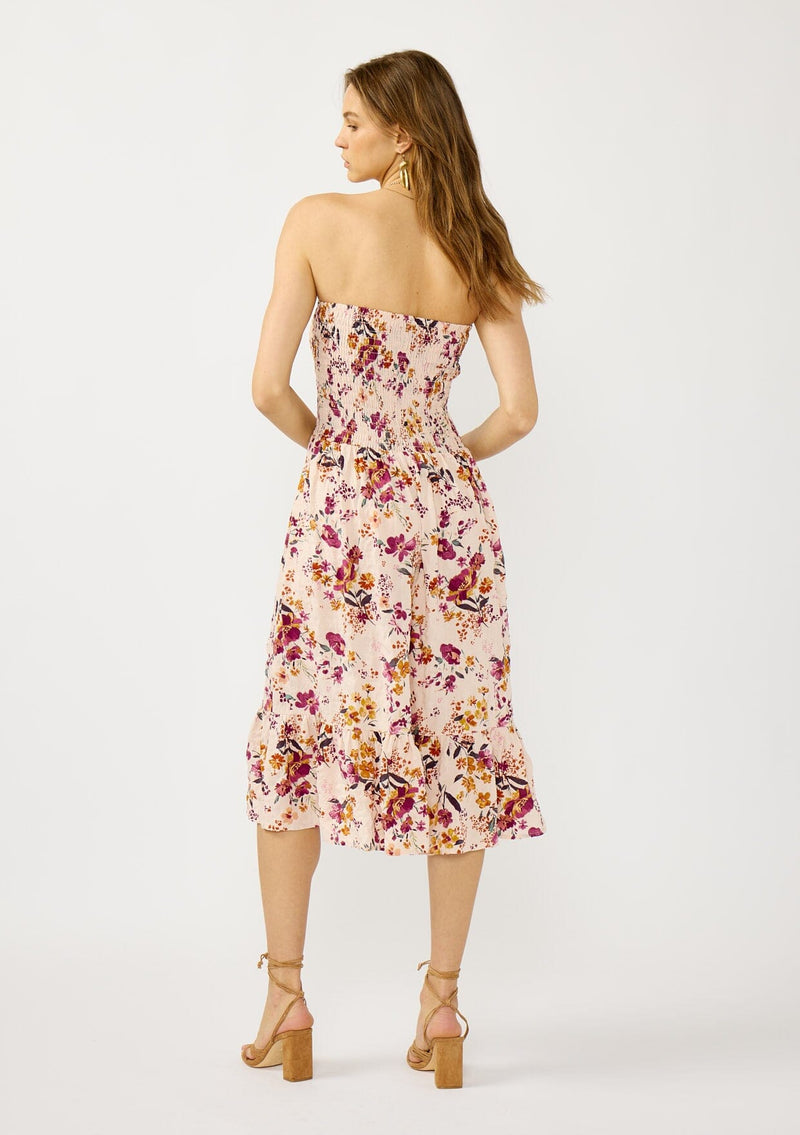 [Color: Almond/Wine] A back facing image of a blonde model wearing a convertible pink floral print midi dress with a smocked bodice and a ruffle trimmed hem. 