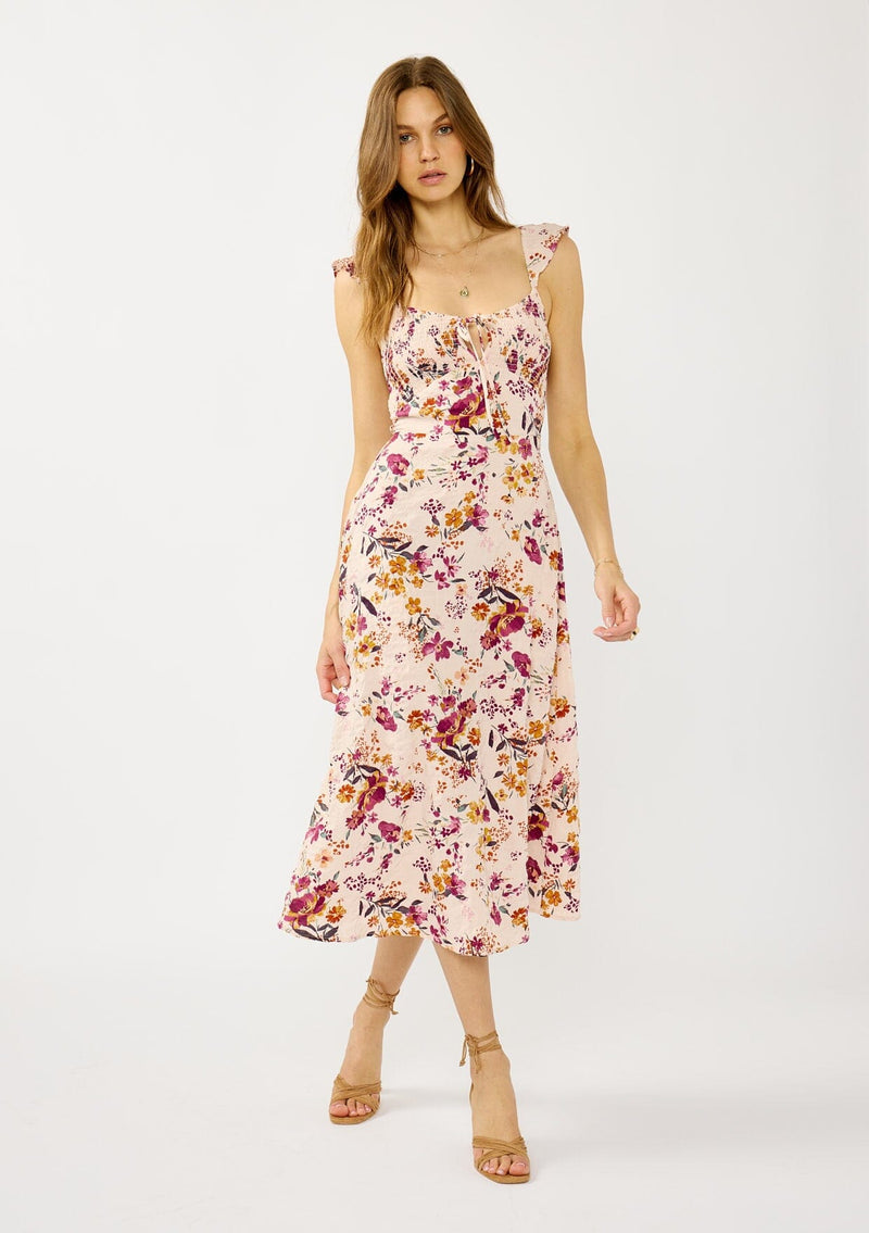 [Color: Almond/Wine] A front facing image of a blonde model wearing a pink floral print midi dress with a scooped neckline, smocked bust and back, elastic shoulder straps with ruffle trim, and sexy cutout back detail. 