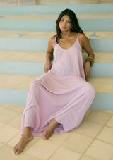 [Color: Orchid] A front facing image of a brunette model wearing an orchid pink sleeveless maxi dress with gold metallic thread details. With adjustable spaghetti straps, a deep v neckline in the front and back, side pockets, and a loose, oversized flowy fit. 