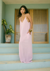 [Color: Orchid] A side facing image of a brunette model wearing an orchid pink sleeveless maxi dress with gold metallic thread details. With adjustable spaghetti straps, a deep v neckline in the front and back, side pockets, and a loose, oversized flowy fit. 