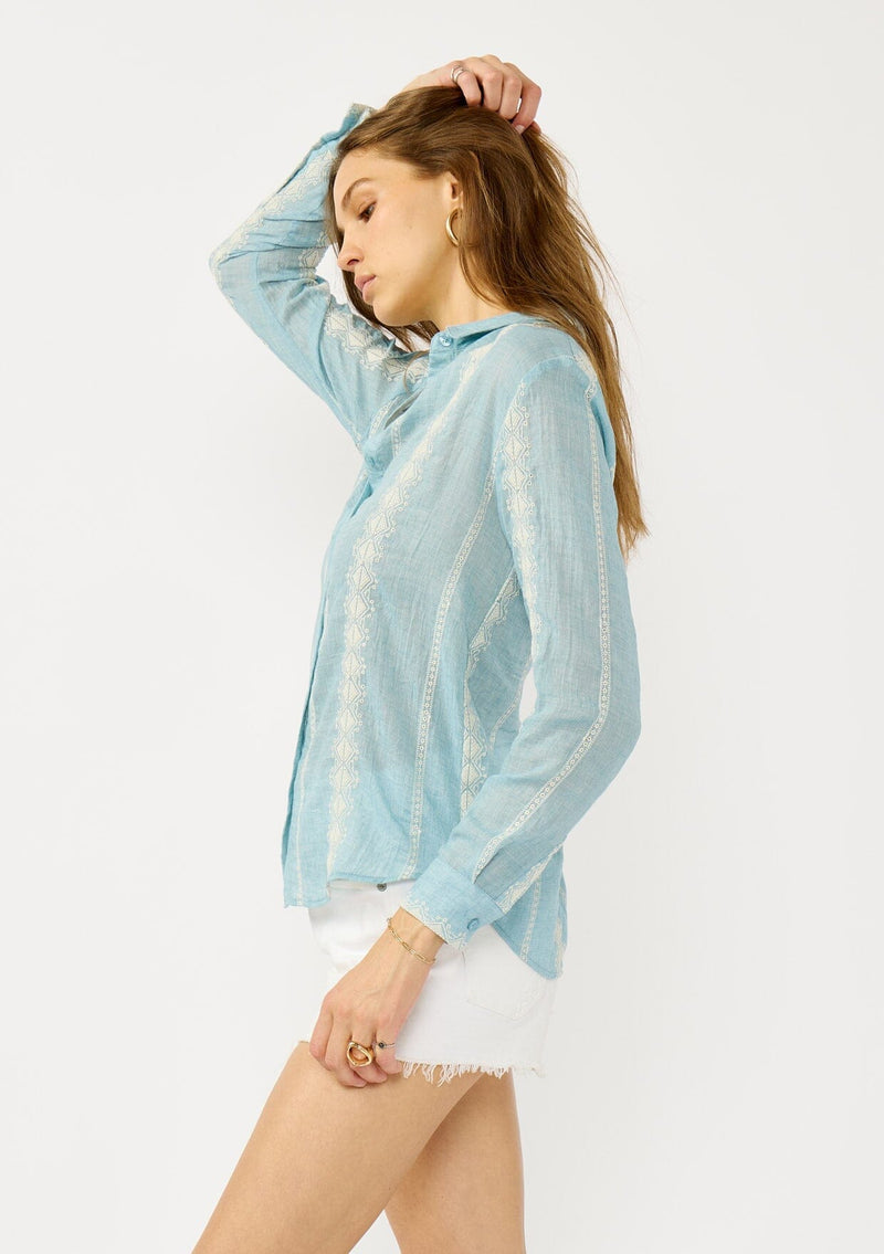 [Color: Light Blue/Ivory] A side facing image of a blonde model wearing a light blue shirt with an embroidered stripe pattern,  a classic collar neckline, and button front. A boho inspired shirt for festivals, casual outings, and country events. 