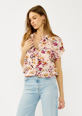 [Color: Almond/Wine] A front facing image of a blonde model wearing a pink floral print top with a button front, twist front detail, and short dolman sleeves. 