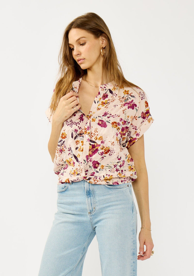 [Color: Almond/Wine] A front facing image of a blonde model wearing a pink floral print top with a button front, twist front detail, and short dolman sleeves. 