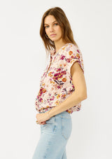 [Color: Almond/Wine] A side facing image of a blonde model wearing a pink floral print top with a button front, twist front detail, and short dolman sleeves. 