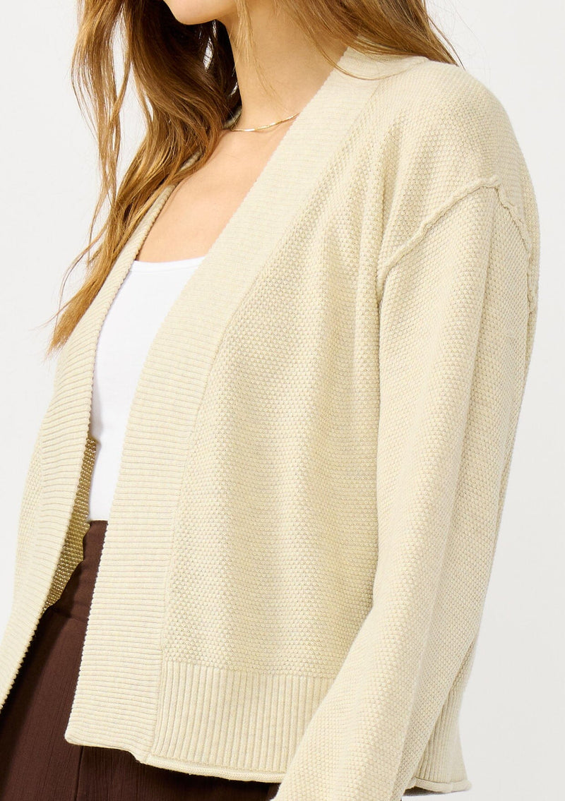 [Color: Heather Natural] A detail image of a blonde model wearing a casual, lightweight cardigan with an open front, ribbed trim, and rolled edges. A classic staple cardigan for transitional styling. 