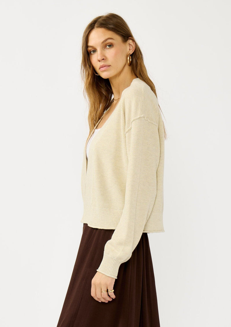 [Color: Heather Natural] A side facing image of a blonde model wearing a casual, lightweight cardigan with an open front, ribbed trim, and rolled edges. A classic staple cardigan for transitional styling. 