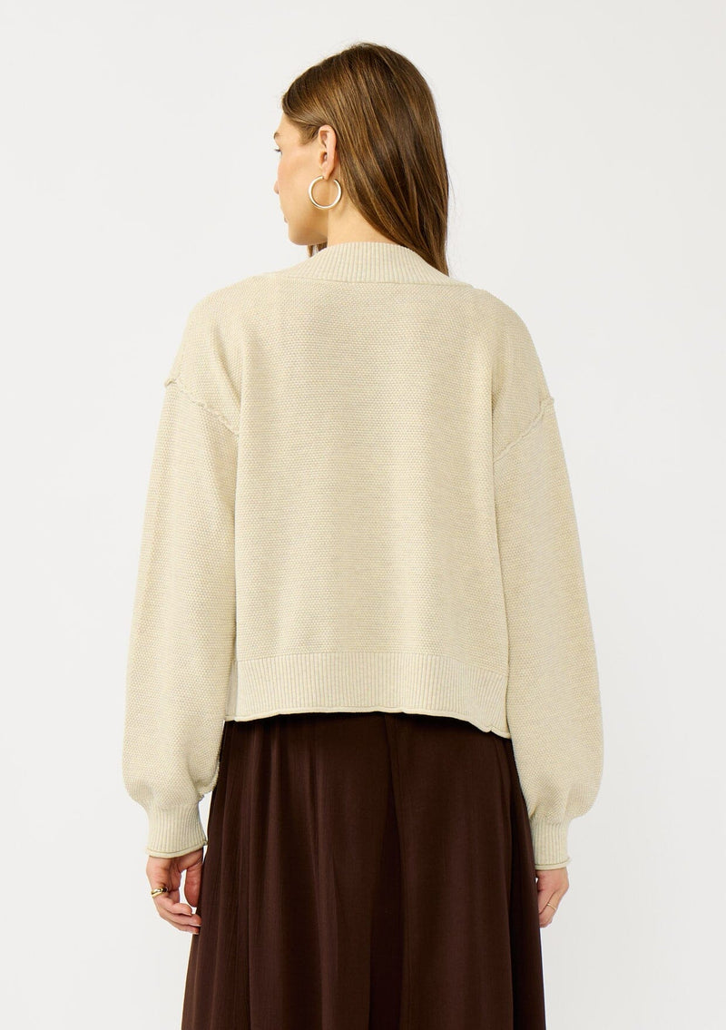 [Color: Heather Natural] A back facing image of a blonde model wearing a casual, lightweight cardigan with an open front, ribbed trim, and rolled edges. A classic staple cardigan for transitional styling. 