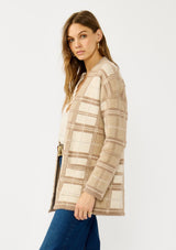 [Color: Tan/Mocha] A side facing image of a blonde model wearing a brown plaid cardigan with cozy long sleeves and an open front. A warm fuzzy sweater for the fall season. 