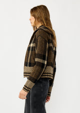 [Color: Brown/Taupe] A side facing image of a blonde model wearing a fall season black and brown plaid jacket with a zip up front and side pockets. 