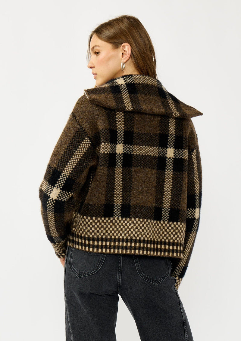 [Color: Brown/Taupe] A back facing image of a blonde model wearing a fall season black and brown plaid jacket with a zip up front and side pockets. 