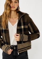 [Color: Brown/Taupe] A detail image of a blonde model wearing a fall season black and brown plaid jacket with a zip up front and side pockets. 
