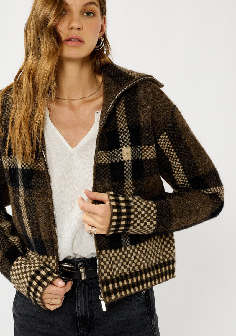 [Color: Brown/Taupe] A detail image of a blonde model wearing a fall season black and brown plaid jacket with a zip up front and side pockets. 