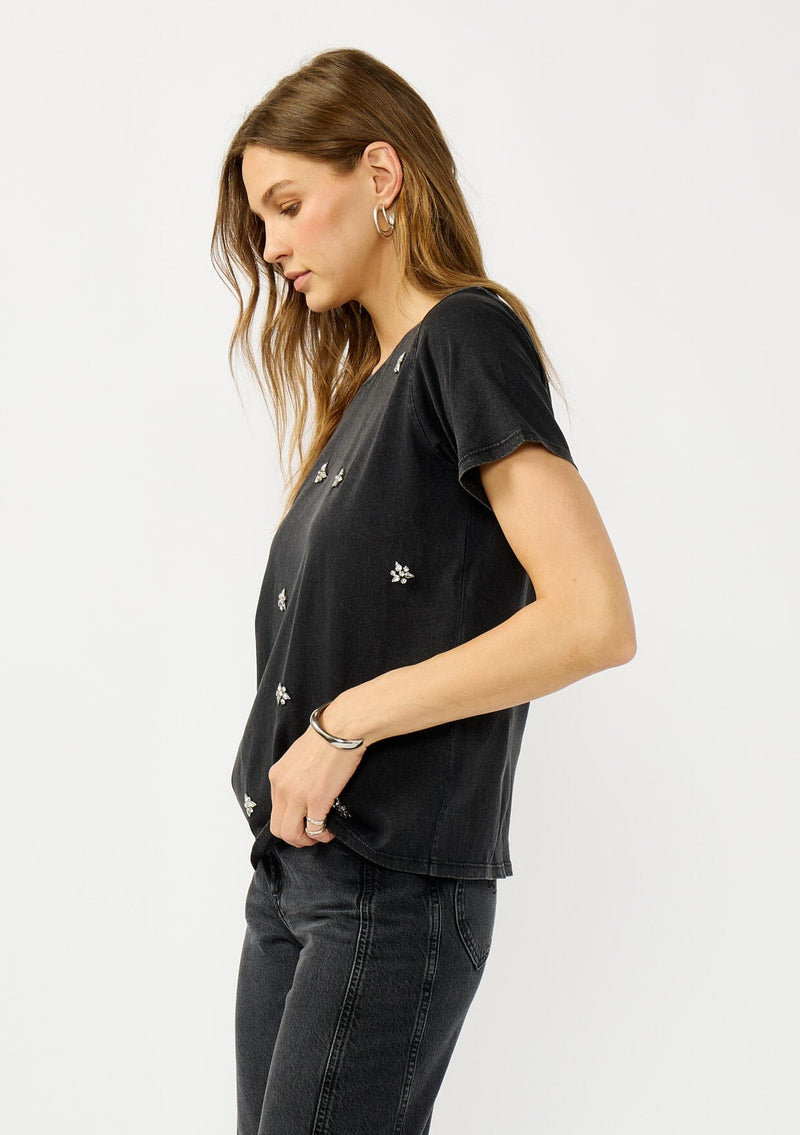 [Color: Charcoal] A side facing image of a blonde model wearing a black vintage wash embellished tee with classic crystal stones. A bold and edgy  statement piece perfect for fall.