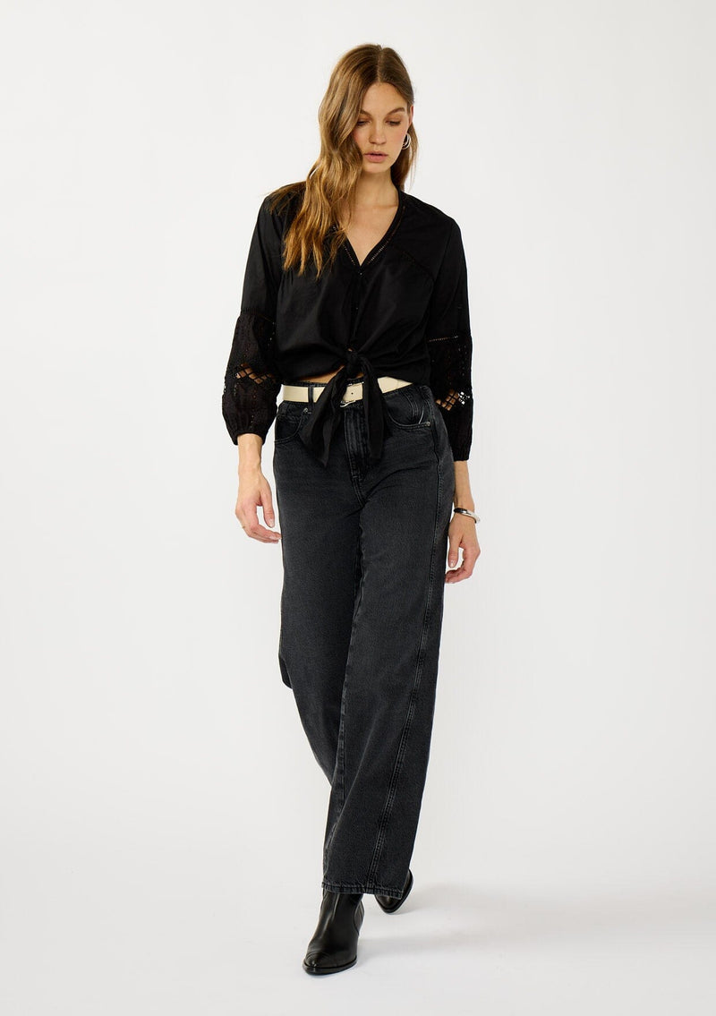 [Color: Black] A front facing image of a blonde model wearing a black lightweight cotton-blend top with a tie front detail, button front, and 3/4 length sleeves with embroidered and cutout details. 