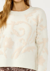 [Color: Ivory/Light Blush] A detail image of a blonde model wearing cozy knit sweater with a floral jacquard pattern. Featuring a classic crew neckline, cozy long sleeves, and ribbed trims. A fall trending sweater for cold weather styling. 