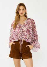 [Color: Mocha/Lilac] A front facing image of a blonde model wearing a billowy purple floral blouse with voluminous sleeves, a ruched front, ruffled v-neckline, and an elastic waist. A flowy chiffon top for the fall season. 