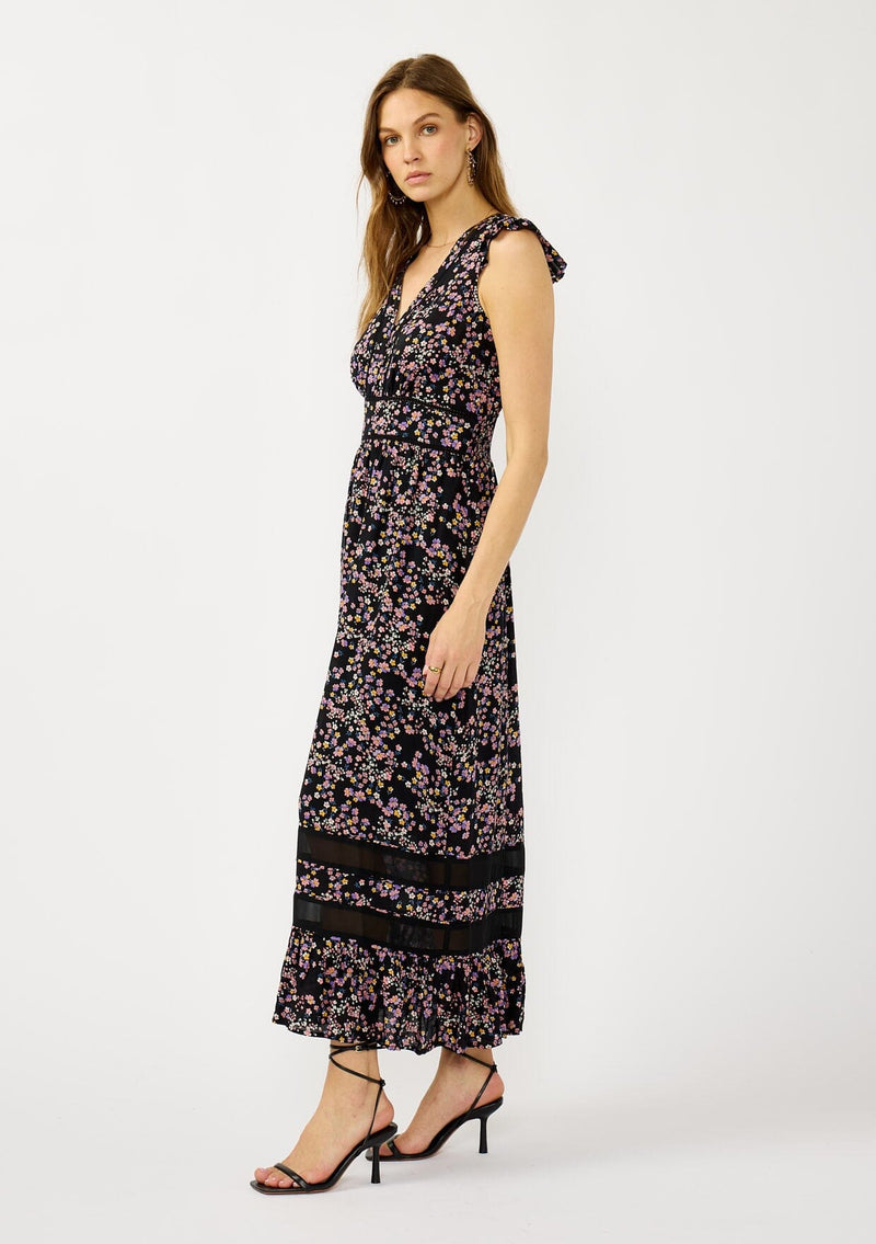 [Color: Black/Pink] A side facing image of a blonde model wearing a black and pink floral print maxi dress with flutter cap sleeves, a v-neckline, button front, smocked back, and sheer tiered layers. A special occasion dress for the fall season. 