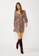 [Color: Natural/Brown] A front facing image of a blonde model wearing a brown paisley mini dress with gold thread details, long sleeves, smocked cuffs, smocked waistline, and a comfortable scooped neckline. A fall bohemian mini dress for casual occasions. 