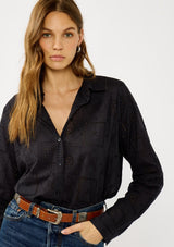 [Color: Graphite] A front facing image of a blonde model wearing a black eyelet shirt with a collared neckline, button front, and button cuff closure.