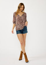 [Color: Natural/Brown] A front facing image of a blonde model wearing a brown paisley blouse with gold metallic threads, a split v-neckline, and 3/4 length sleeves with ruffled elastic cuffs. A relaxed boho top for the fall season. 