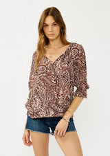 [Color: Natural/Brown] A front facing image of a blonde model wearing a brown paisley blouse with gold metallic threads, a split v-neckline, and 3/4 length sleeves with ruffled elastic cuffs. A relaxed boho top for the fall season. 