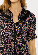 [Color: Black/Pink] A detail image of a black and pink floral print top with puff sleeves, a split v-neckline with ties, shirred details, and lace trims. A day to night versatile top for the fall season. 