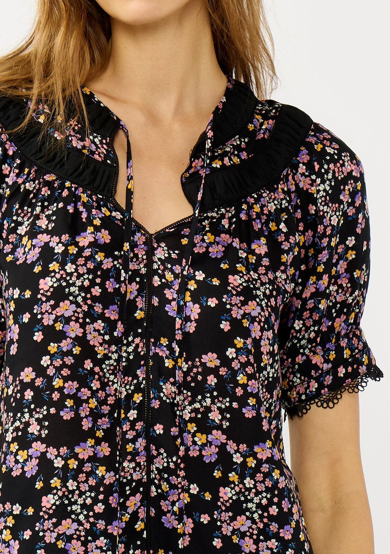 [Color: Black/Pink] A detail image of a black and pink floral print top with puff sleeves, a split v-neckline with ties, shirred details, and lace trims. A day to night versatile top for the fall season. 