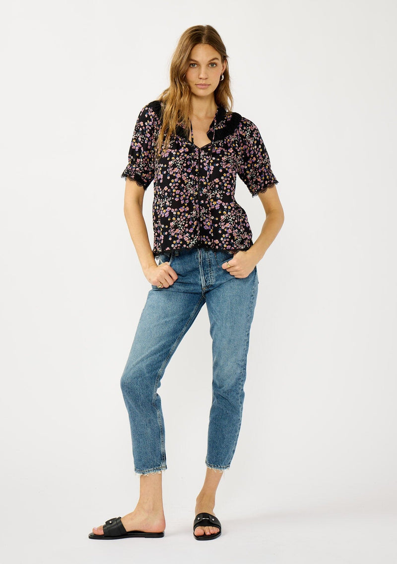 [Color: Black/Pink] A front facing image of a black and pink floral print top with puff sleeves, a split v-neckline with ties, shirred details, and lace trims. A day to night versatile top for the fall season. 