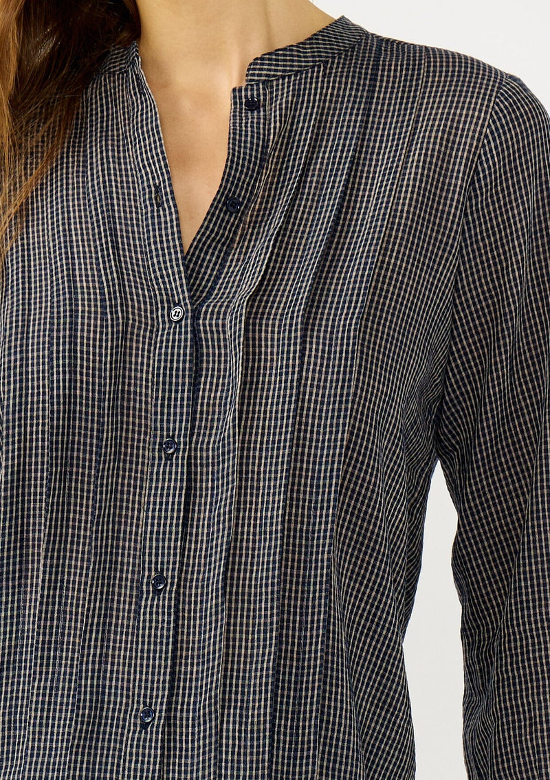 [Color: Navy/Taupe] A detail image of a blonde model wearing a dark navy checkered blouse with a round neckline, button front, and center front pintuck details. A casual fall piece with a polished touch for work and casual outings. 