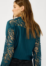 [Color: Teal] A back facing image of a blonde model wearing a striped jacquard teal shirt with lace cutouts, a button front, and collared neckline. A cool and polished blouse for the fall season. 