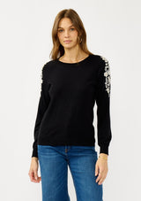 [Color: Black] A front facing image of a blonde model wearing a black pullover sweater with pearl embellishment on the shoulder. A classic and feminine sweater for the fall season. 