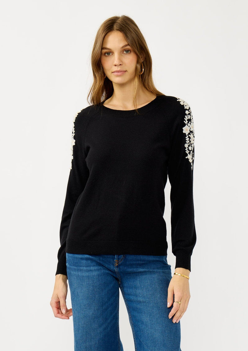 [Color: Black] A front facing image of a blonde model wearing a black pullover sweater with pearl embellishment on the shoulder. A classic and feminine sweater for the fall season. 
