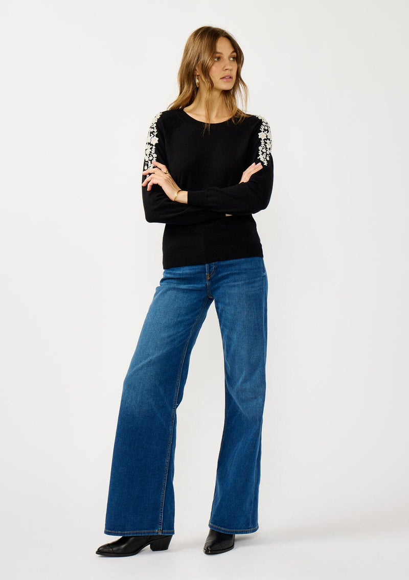 [Color: Black] A front facing image of a blonde model wearing a black pullover sweater with pearl embellishment on the shoulder. A classic and feminine sweater for the fall season. 