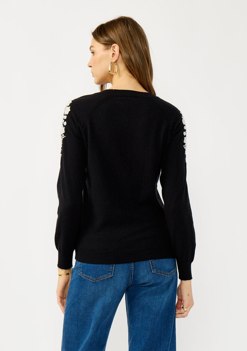 [Color: Black] A back facing image of a blonde model wearing a black pullover sweater with pearl embellishment on the shoulder. A classic and feminine sweater for the fall season. 