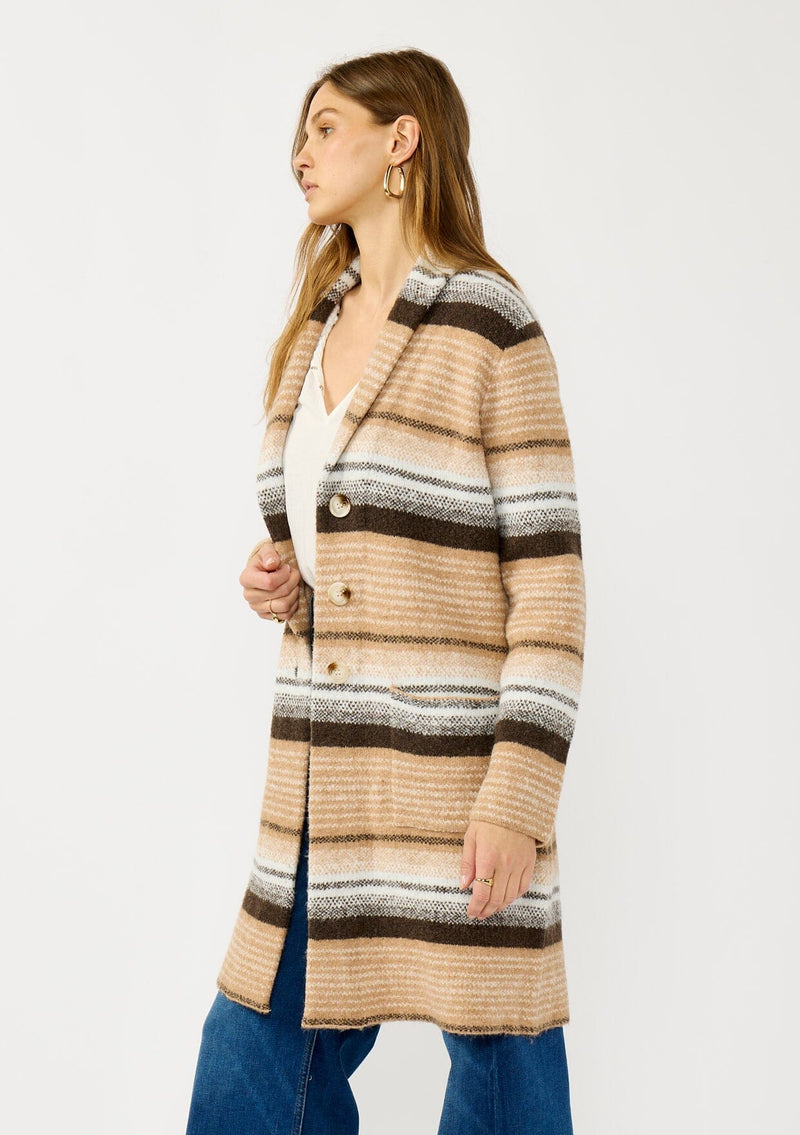 [Color: Camel/Brown] A side facing image of a blonde model wearing a brown and tan striped mid length coatigan with a shawl collar, button front, and side patch pockets. Effortlessly cozy for the fall and winter season. 
