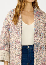 [Color: Mauve/Natural] A detail  image of a blonde model wearing a mauve pink floral bohemian jacket with an oversized fit, long sleeves, crochet trim, and side pockets. 